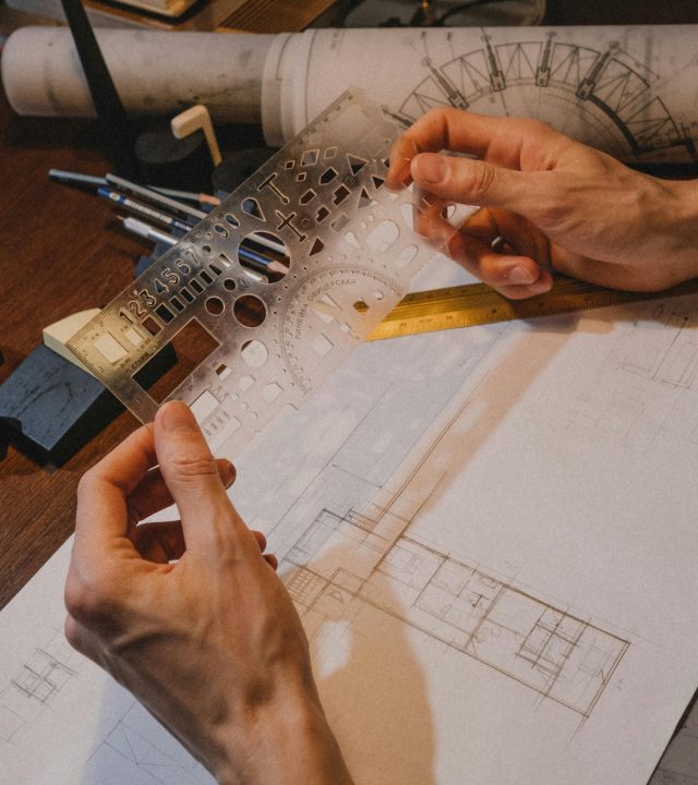 Close-up of hands using a stencil for architectural drawing, indoors on a wooden desk.
